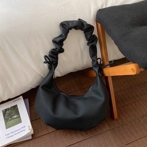 Detail einer schwarzen Halbmond-Tasche mit gefaltetem Griff auf Holzboden