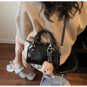 Detail of black shell bag with ciho 2ad embossing and cute teddy bear charm on model