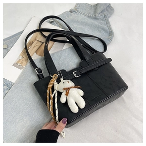 Detail of black leather bucket bag with cute bear charm and fashion silk ribbon decoration
