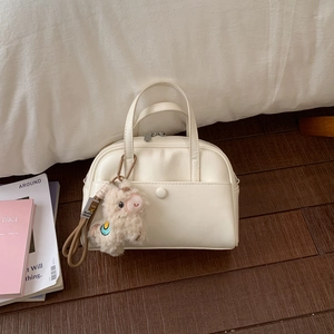Detail of off-white Boston bag with plush alpaca charm on a dark wood floor