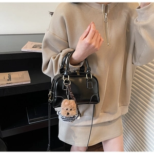 Detail of black glossy shell bag with dual handles and a cute dog plush charm detail