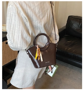 Detailed shot of dark brown glossy bucket bag with wooden bead charm and brand logo