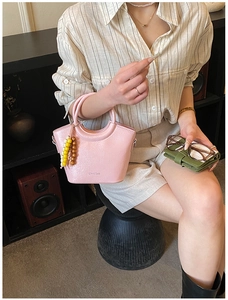 Detailed shot of pink glossy leather handbag with beaded charm and arc-shaped top handle