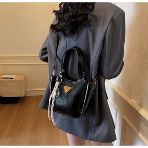 Détail d'un sac à main en cuir noir brillant avec emblème et accessoire tressé décoratif