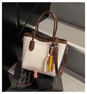 Detail der cremefarbenen Beuteltasche mit braunem Rand und dekorativem Holzperlen-Anhänger