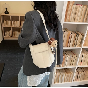 Detailansicht der cremefarbenen Ledertasche mit Bärenanhänger getragen zum grauen Blazer