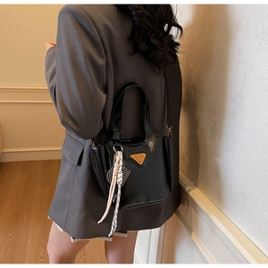 Détail du sac en cuir verni brillant avec logo en métal triangulaire et breloque tressée