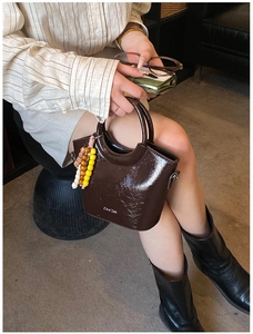 Detail of a dark brown patent leather bucket bag with a round handle and beaded charm