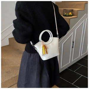 White bucket bag with round handle and beaded tassel detail shown in interior scene