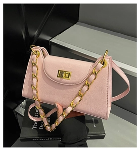 Close-up of pink lychee grain leather bag with gold chain and turn-lock on dark books