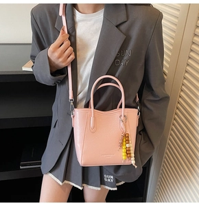 Detail der hellrosa Beuteltasche mit Perlenanhänger und Schultergurt am Modell