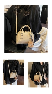 Detail of creamy white leather handbag with dual top zippers and plush bear charm