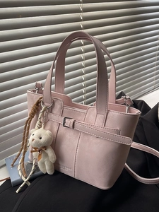 Pink PU leather bucket bag with top handle and bear charm against a minimalist background