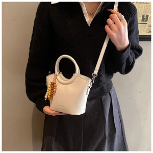 Close-up of beige leather bucket bag with circular handle and multi-color beaded charm