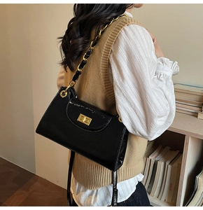 Detail of black patent leather chain bag with golden swivel lock on a female model
