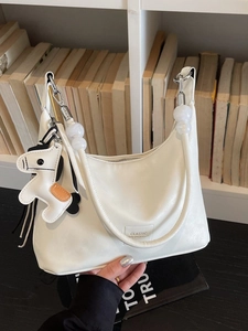 Sac hobo blanc minimaliste avec poignée en perles et breloque cheval dans un décor de bibliothèque