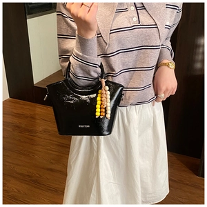 Detail of black glossy patent leather bucket bag with short handle and beaded charm
