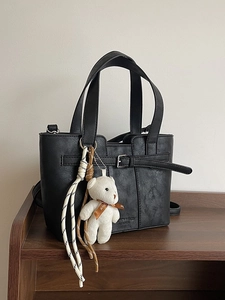 Black bucket tote bag in lychee texture with bear charm on dark wooden surface