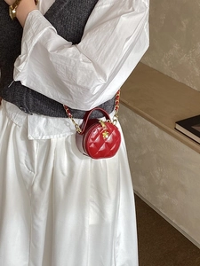 Mini sac rond rouge matelassé avec bandoulière chaîne dorée porté par un mannequin