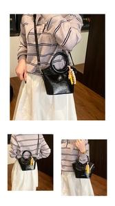 Detail of black glossy bucket bag with circular handle and colorful beaded charm