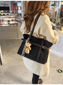 Detail of large black tote bag featuring brown straps and a cute plush bear charm