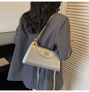 Detail of silver pleated texture shoulder bag with gold chain strap on grey blazer