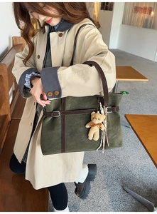 Detail view of deep green suede tote bag with brown leather straps and plush bear charm