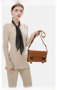 Close-up of brown leather messenger bag with double buckle straps and orange webbing details
