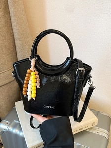 Chic black patent leather bucket bag with top handle, crossbody strap and beaded charm