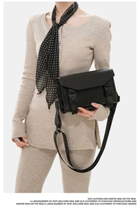 Detailed view of men's black messenger bag with flap and dual buckle closure worn by a model