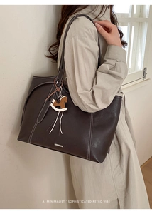 Detail of dark brown tote bag featuring white contrast stitching and a wooden horse charm