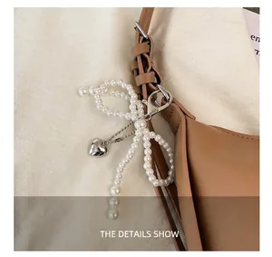 Detail of a brown leather bag with pearl bow charm and silver heart pendant hardware