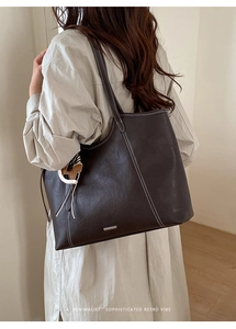 Macro detail of large brown tote bag with white contrast stitching and horse charm