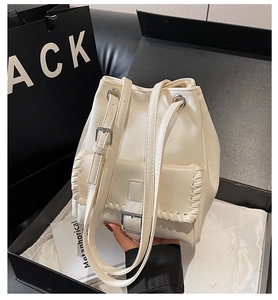 Detail of cream bucket bag with woven edges and metal buckle in a luxury gift box