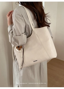 Close-up of cream tote bag featuring a cute horse charm and luxury metal logo tag