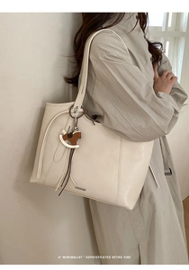 Detail of minimalist cream tote bag with elegant horse charm on a grey trench coat