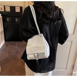 Détail d'un sac seau en cuir blanc avec bords tressés porté au dos par un mannequin