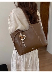 Brown leather tote bag with contrast stitching and horse charm worn by a model