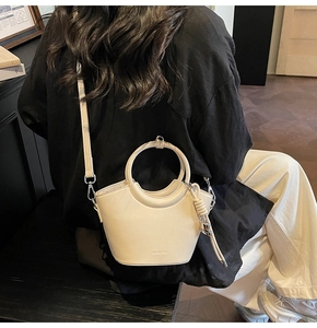 Détail du sac seau crème montrant la poignée ronde, la sangle nouée et le logo