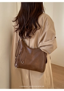 Rear view of a large brown leather tote bag worn as a shoulder bag in a minimalist setting