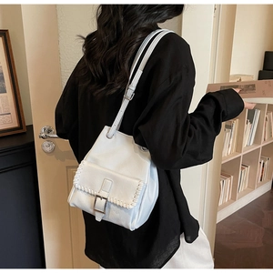 Sac seau vintage en cuir blanc avec coutures tressées porté à l'épaule par un mannequin