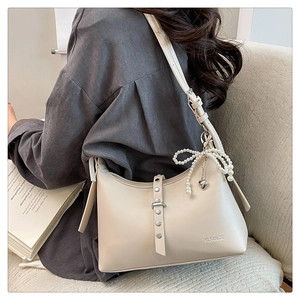 Detail view of cream dumpling bag featuring a pearl bow charm and metal stud hardware