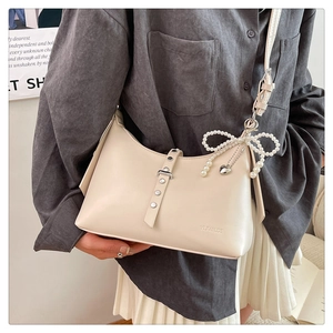 Chic dumpling bag in off-white leather with pearl bow and heart charm on female model