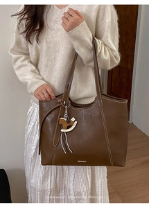 Detail of deep brown tote bag featuring white contrast stitching and a wooden horse charm