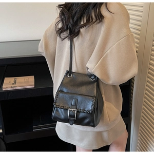 Detail of black bucket bag featuring woven stitching and metal buckle on a model