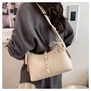 Detail of cream leather shoulder bag featuring a pearl bow and heart charm on the zipper
