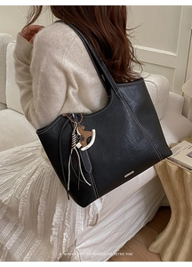 Detail of black leather tote bag featuring white contrast stitching and a wooden charm