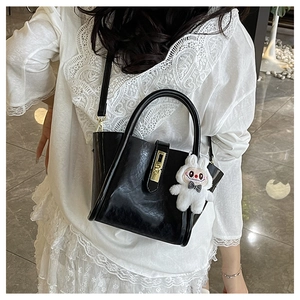 Détail d'un sac seau en cuir noir avec fermoir doré et breloque lapin sur un modèle