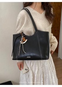 Detail of black tote bag with white stitching, smooth leather texture and horse charm