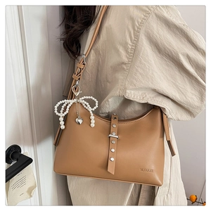 Detail of a brown leather shoulder bag featuring a pearl bow and heart metal pendant